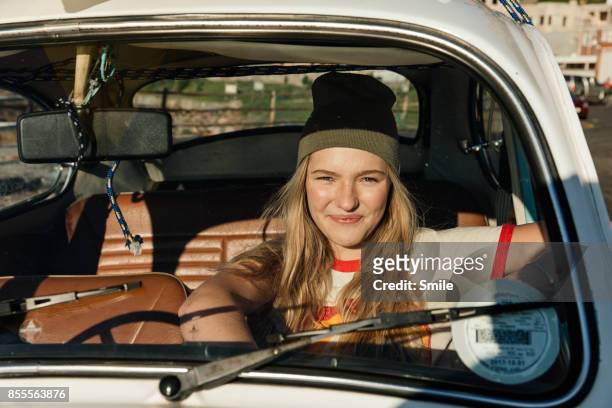 young woman sitting in car smiling - ruitenwisser stockfoto's en -beelden