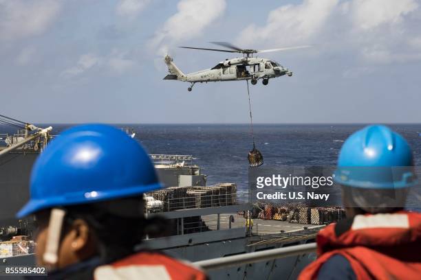 In this U.S. Navy handout, sailors aboard the amphibious assault ship USS Kearsarge observe as an MH-60 Sea Hawk helicopter transfers pallets of...