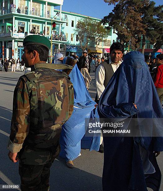 Burqa-clad Afghan women walk past an Afghan National Army soldier on watch in front of the Hazrat Ali Shrine in the northern town of Mazar-i-Sharif...