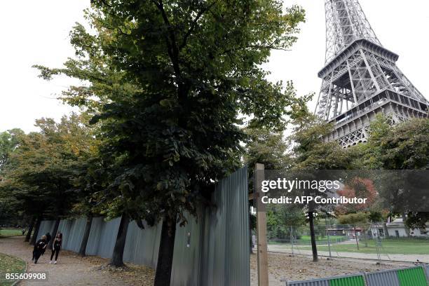 People walk by the metal gates set up for the construction of bulletproof glass walls set to go up around the Eiffel Tower, on September 29 in Paris....