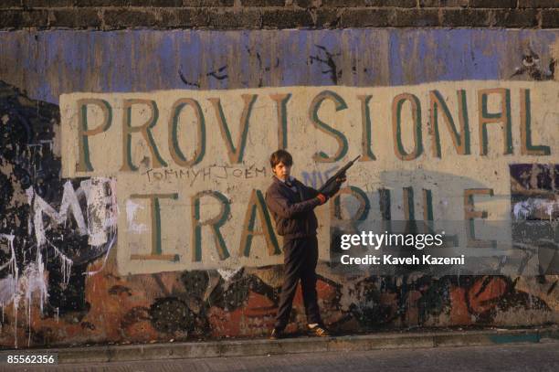 Boy with a toy gun stands in front of a Provisional IRA mural in the heart of the Catholic and Republican community of west Belfast, 15th September...