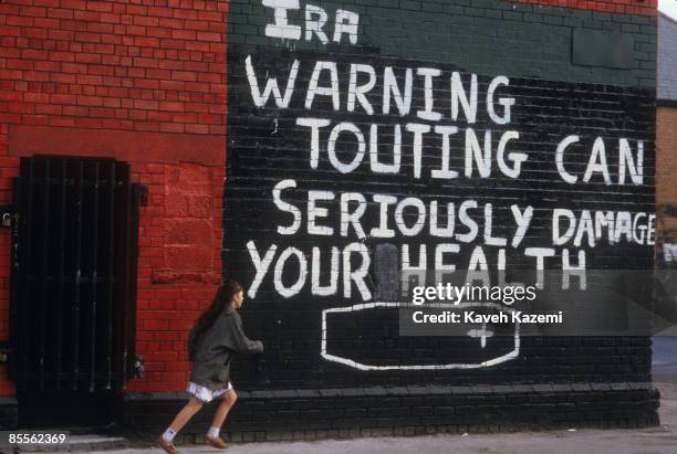 Young girl runs past a mural on the corner of The Falls Road in west Belfast with an IRA warning for informers who betray the nationalist community,...