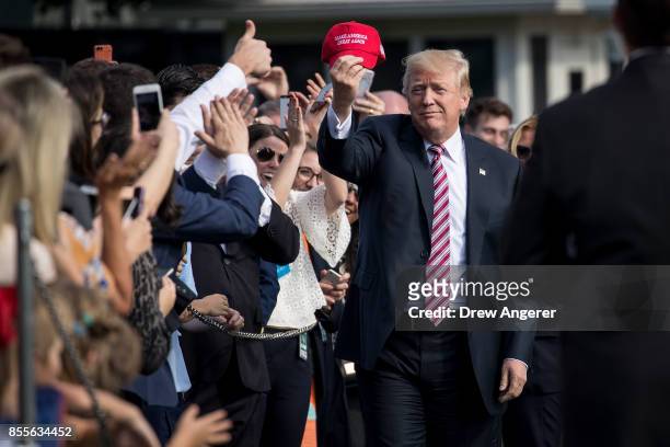 President Donald Trump holds up a 'Make America Great Again' hat while greeting onlookers before boarding Marine One on the South Lawn of the White...
