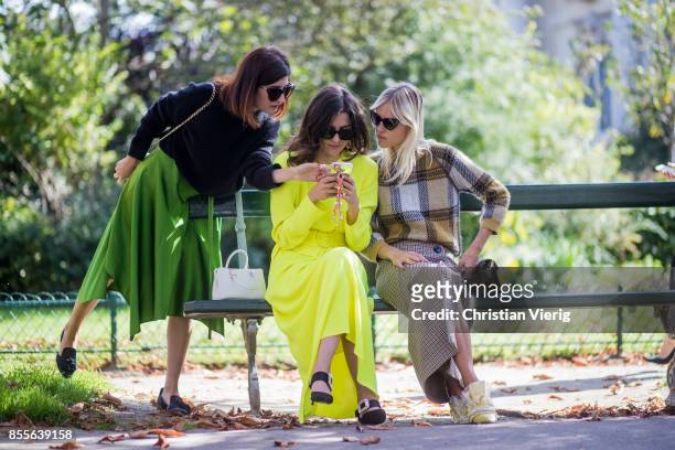 Valentina Siragusa and Eleonora Carisi wearing neon dress and Linda Tol sitting on a bench looking at a mobile phone seen outside Issey Miyake during...