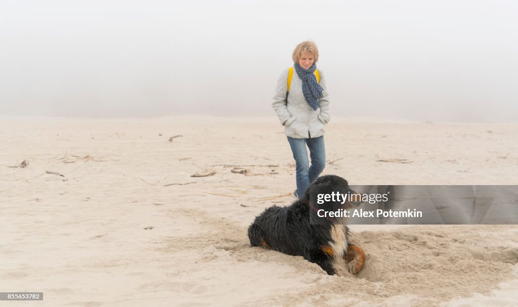 Attractive mature woman walking the dog щи the sandy beach of the Baltic Sea