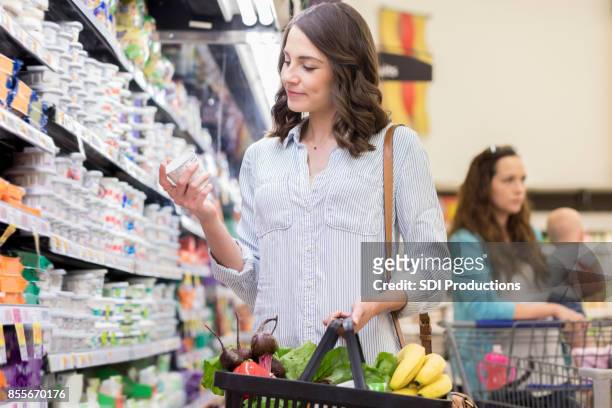 confident woman reads label on a yogurt container - nutrition label stock pictures, royalty-free photos & images