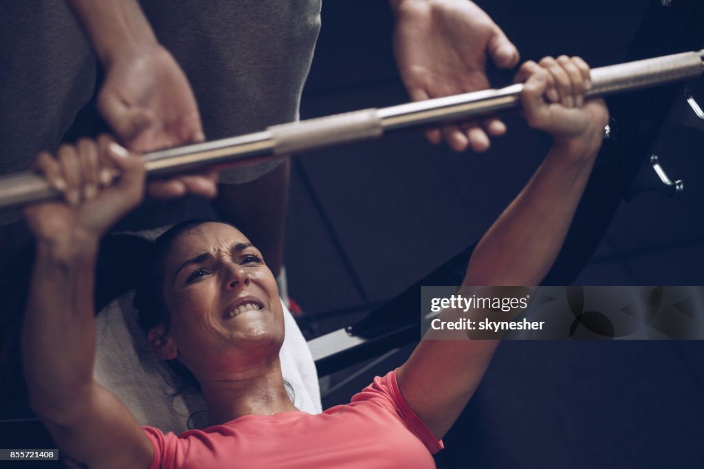 Determined athlete making an effort while doing bench press exercises with her coach.