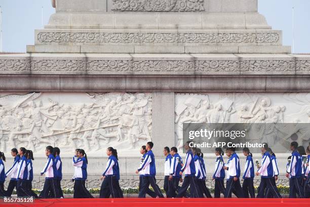 Youths walk past sculpted scenes from China's revolution on the Monument to the People's Heroes in Tianmanmen Square during a ceremony to mark...