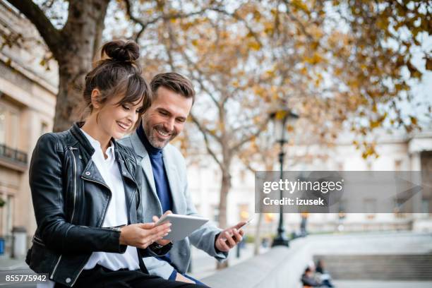 mooie paar met behulp van digitale tablet op trafalgar square in londen, herfst seizoen - destination fashion 2016 stockfoto's en -beelden