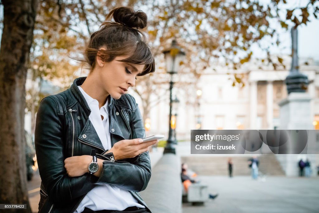 Orolig kvinna använder smart telefon på Trafalgar Square i London, höstsäsongen