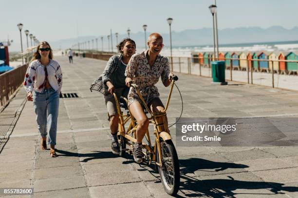 couple riding on a tandem bicycle on the boardwalk - tandem bicycle foto e immagini stock