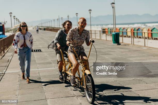 couple riding on a tandem bicycle on the boardwalk - tandem bicycle stockfoto's en -beelden