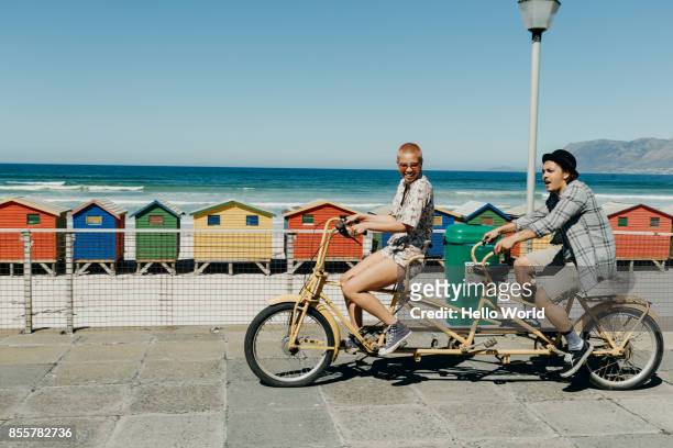 Young couple riding a tandem bicycle on a boardwalk