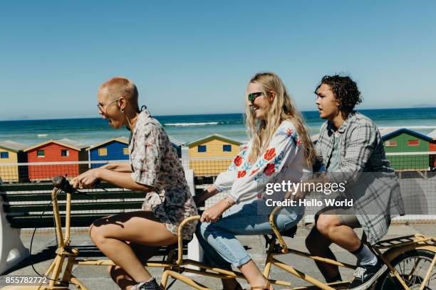 three friends laughing on a tandem bicycle on a boardwalk - south african culture photos et images de collection