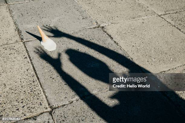Shadow of a person's arms reaching for a fallen ice-cream cone