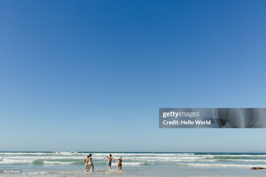 Friends running in the waves. Wide shot