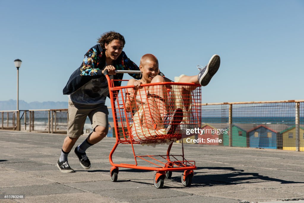 Young man pushing girl in red trolley