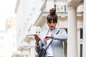 Worried woman standing with smart phone in front of city house