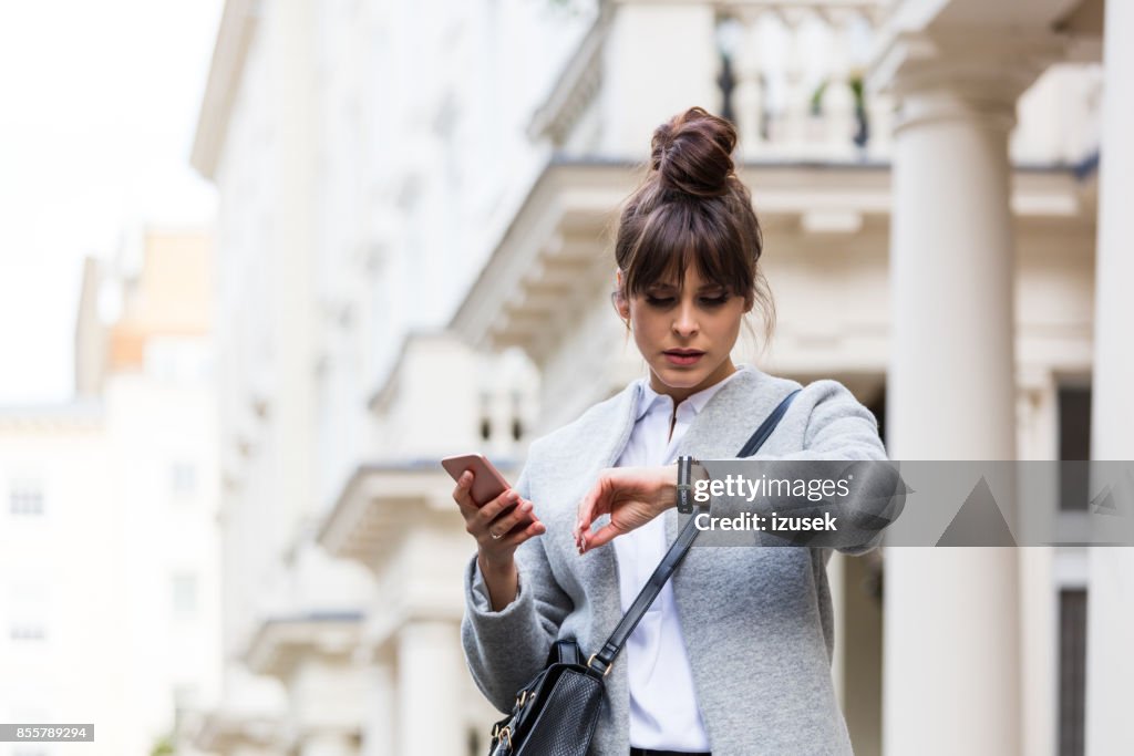 Worried woman standing with smart phone in front of city house