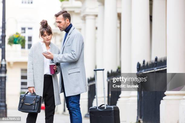 elegante paar stehen in der stadt straße, mann mit handy - suitcase couple stock-fotos und bilder