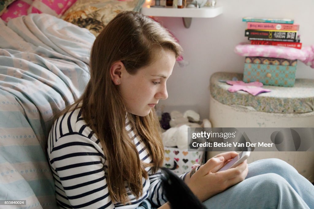 Teenager sitting in her bedroom, texting on mobile phone.