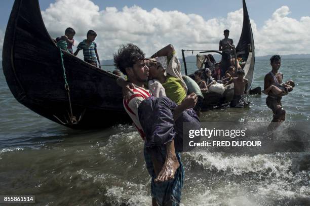 Bangladeshi man helps Rohingya Muslim refugees to disembark from a boat on the Bangladeshi shoreline of the Naf river after crossing the border from...