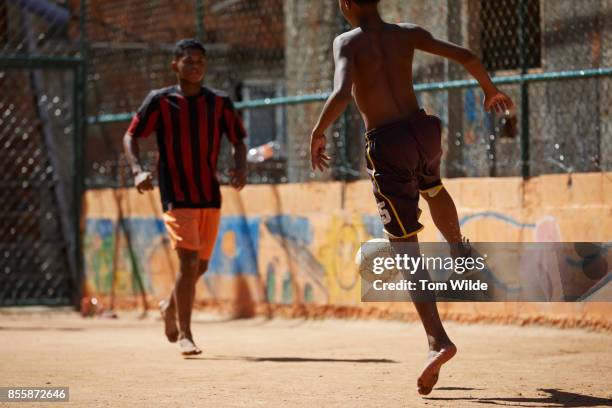 two young men playing football on a dirt court - favela stock pictures, royalty-free photos & images