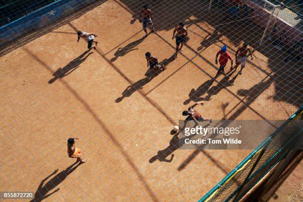 overhead shot of a group of young men playing football on a dirt court - slum stock pictures, royalty-free photos & images