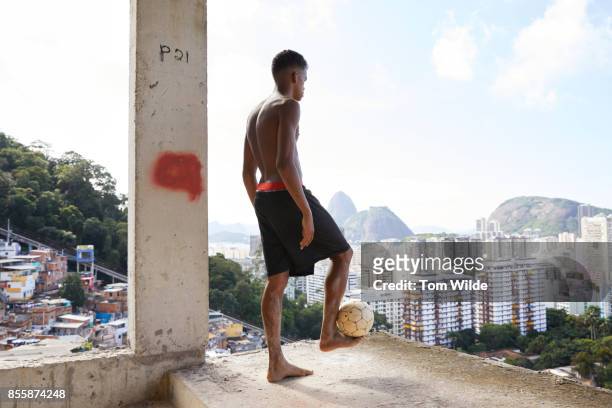 young man standing with a football balanced on his foot with the city of rio in the background - favela 個照片及圖片檔