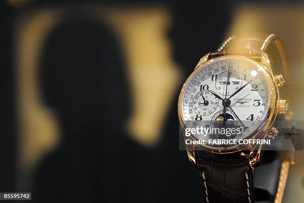 Visitors are seen in silhouette behind a Longines watch during the press day at the Baselworld 2009 watch and jewellery show on March 25, 2009 in...