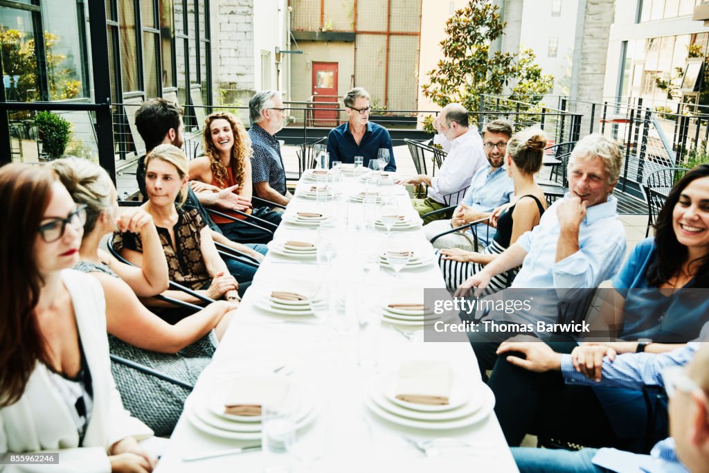 Group of friends in discussion while seated for celebration meal at table on outdoor patio