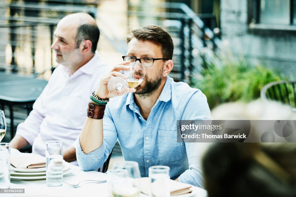 Man drinking wine while sharing dinner with friends on restaurant patio