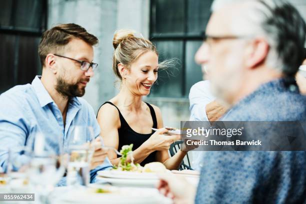 smiling woman passing platter of food to friend during celebration dinner on outdoor patio - mature men group stock pictures, royalty-free photos & images