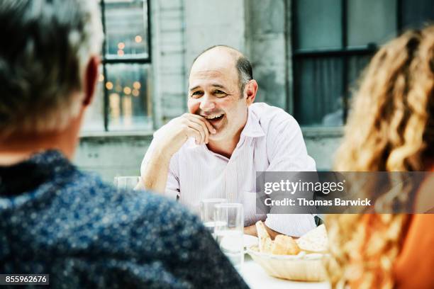 laughing man in discussion with friends during celebration dinner - bald head stock pictures, royalty-free photos & images