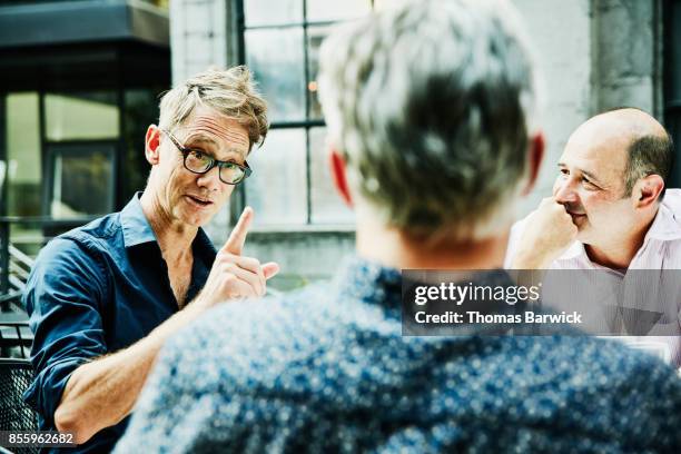 smiling man in discussion with friends during celebration meal on outdoor patio - friends talking cafe stock pictures, royalty-free photos & images