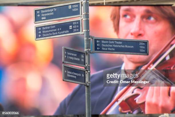 Street sign stands before a large screen showing a musician in a free, open-air performance of Beethoven's 9th Symphony and "The Ode To Joy" at...