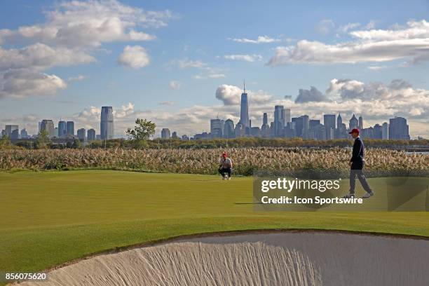 Golfers Patrick Reed and Jordan Spieth putt on the 10th hole with the New York city skyline in the background during the third round of the...