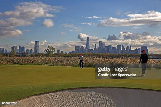 Golfers Patrick Reed and Jordan Spieth putt on the 10th hole with the New York city skyline in the background during the third round of the...