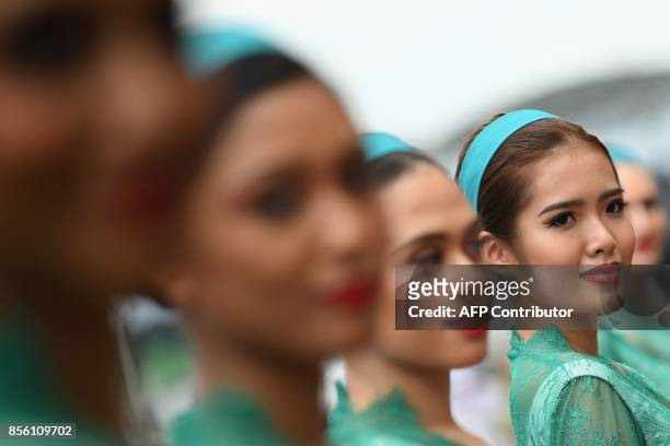 Grid girls pose for photographs before the start of the Formula One Malaysia Grand Prix in Sepang on October 1, 2017. / AFP PHOTO / MANAN VATSYAYANA