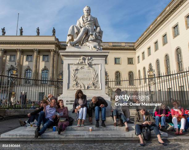 People sit under a statue of Alexander von Humboldt as they wait for the beginning of a free, open-air concert conducted by Daniel Barenboim in which...