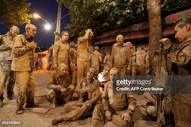 Iranian Shiite Muslims sit after rubbing mud on their body during the 'Kharrah Mali' ritual to mark the Ashura religious ceremony in the city of...