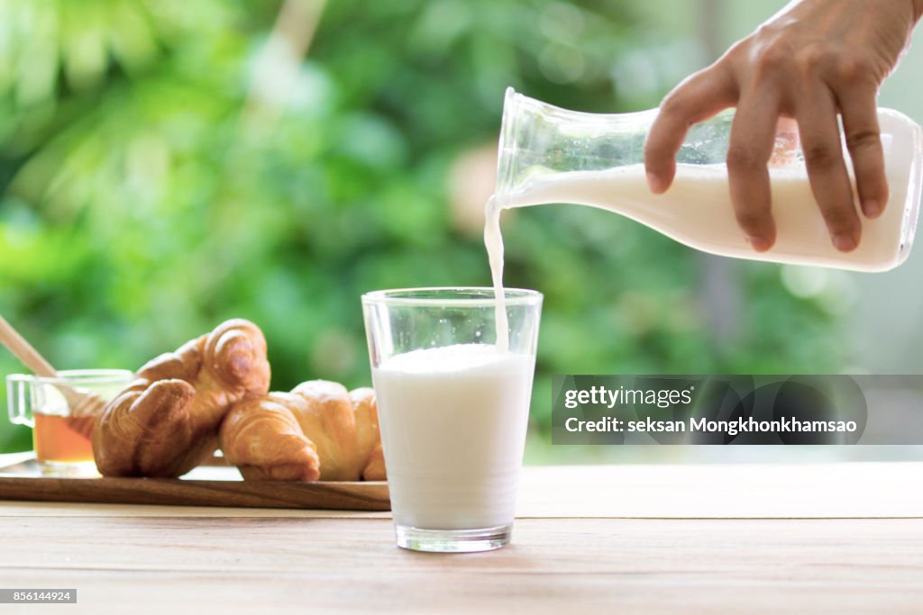 The hand of a boy on a sunny day in the garden pours milk in a transparent cup where milk falls in slow motion . concept of healthy food and breakfast of milk and biscuits or cookies