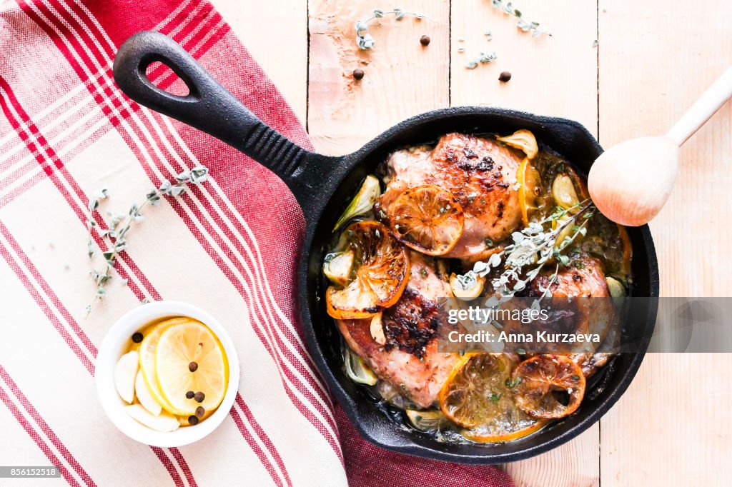 Homemade roasted chicken with lemon and garlic in a pan on a wooden table, top view