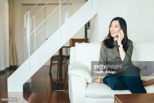 young woman talking on cell phone on the sofa in living room - answering stock-fotos und bilder