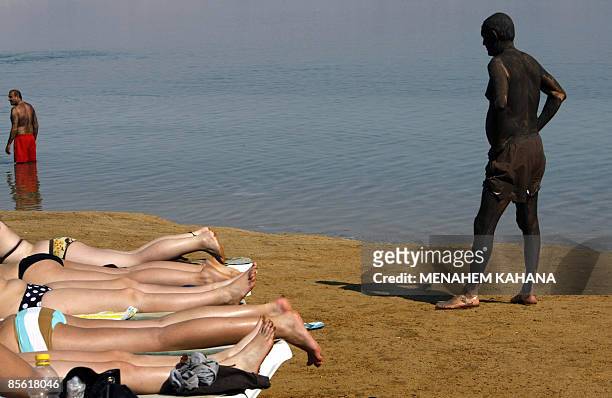 Tourists enjoy a sunny day as one covers his body with mineral-rich mud on the shore of the Dead Sea at Ein Bokek in Israel, on March 26 , 2009. AFP...