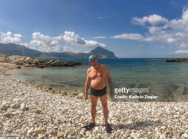 happy senior man on pebbly beach, wearing goggles and fins - chubby swimsuit stock pictures, royalty-free photos & images
