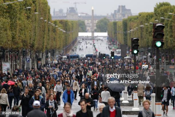 People walk down the Champs Elysees avenue during a "car free" day in Paris on October 1, 2017. Parisians were encouraged to roller-blade, bike or...