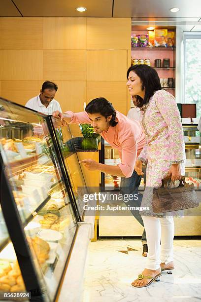 couple looking at food in display case - bakery display stock-fotos und bilder