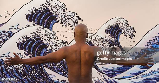 man with arms outstretched against wave mural - katsushika hokusai stock pictures, royalty-free photos & images