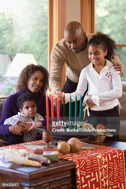 girl lighting kwanzaa candles with family - kwanzaa fotografías e imágenes de stock